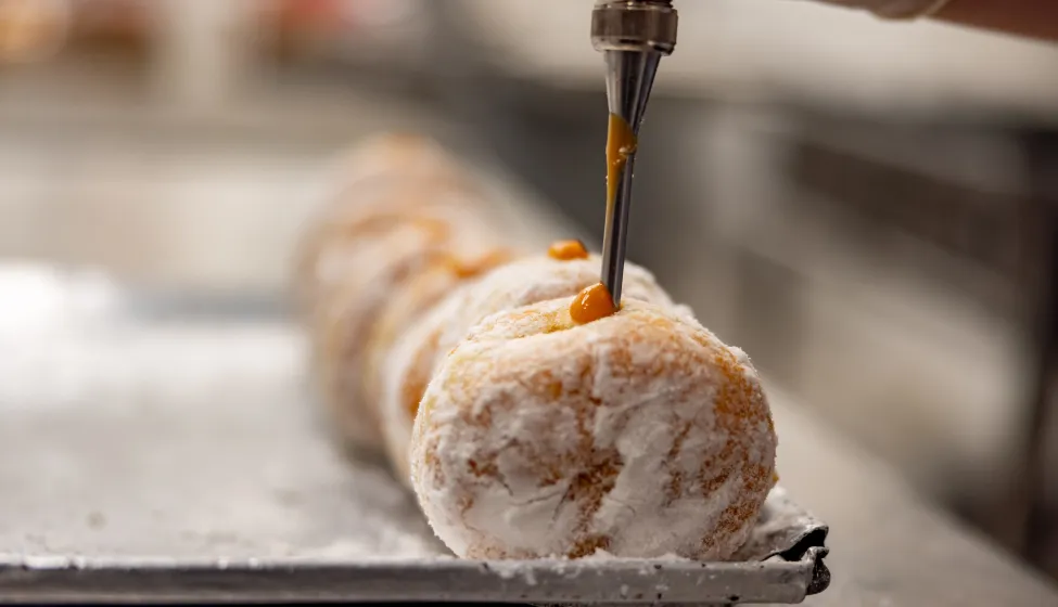 Close-up on a baker filling donuts with a caramel sauce at an industrial bakery - business concepts