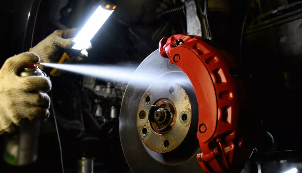 Car mechanic in gloves holding lamp and spraying disc brake fluid in garage