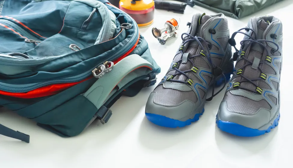 Hiking gear and camping equipment for travel on white background, backpack, hiking boots, rain jacket, and portable cooking equipment.