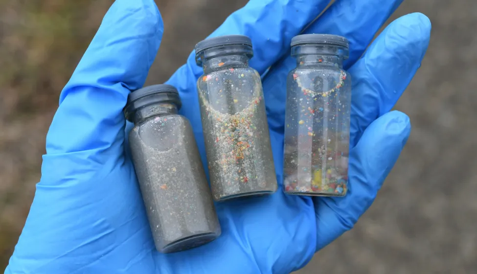 A gloved hand holding vials of water samples to test for pollution and plastic contamination