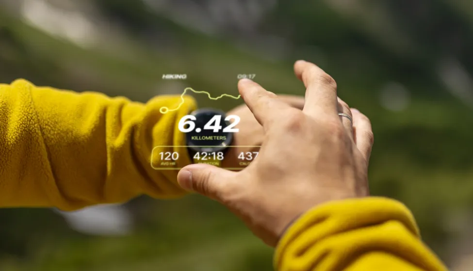Close-up view of a person using augmented reality technology outdoors, displaying hiking statistics. The background features a blurred natural setting, emphasising innovation and adventure in an outdoor environment.