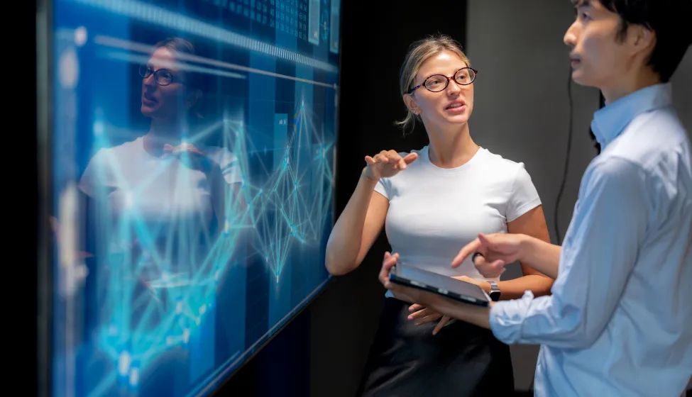 Business meeting in modern office with female programmer explaining infographic on screen to Japanese manager. Teamwork, strategy, innovation, coding, big data, AI, and technology presentation for success.