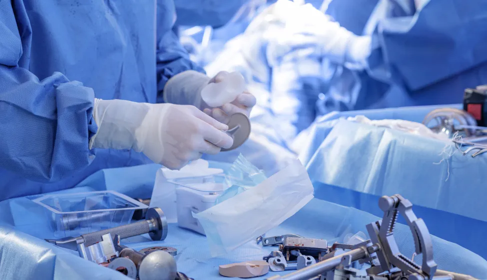 Surgeon prepares knee implant and tools on sterile blue drapes during total knee arthroplasty, showing modern OR workflow and equipment.