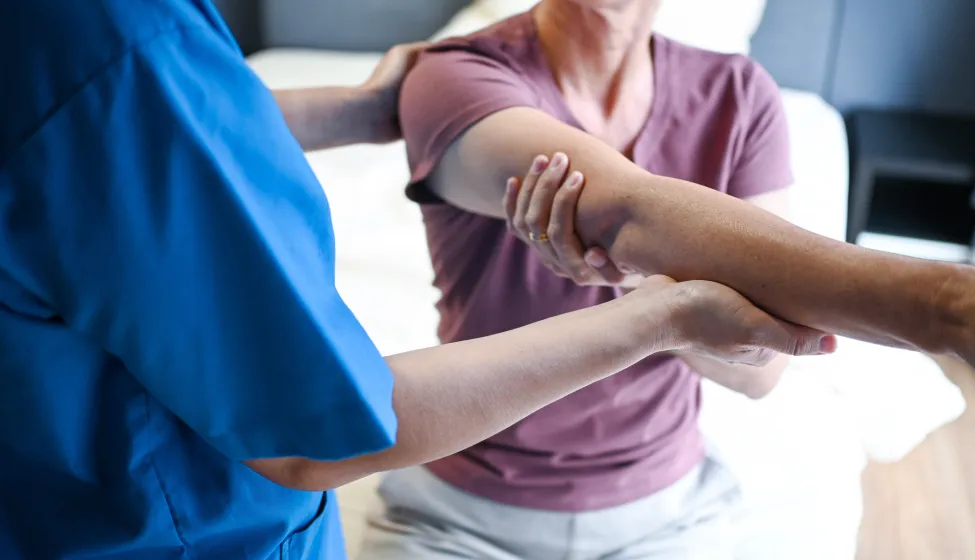 A caring physiotherapist helps an older woman perform structured arm rehabilitation exercises, ensuring proper technique and encouraging progress throughout the healing process.