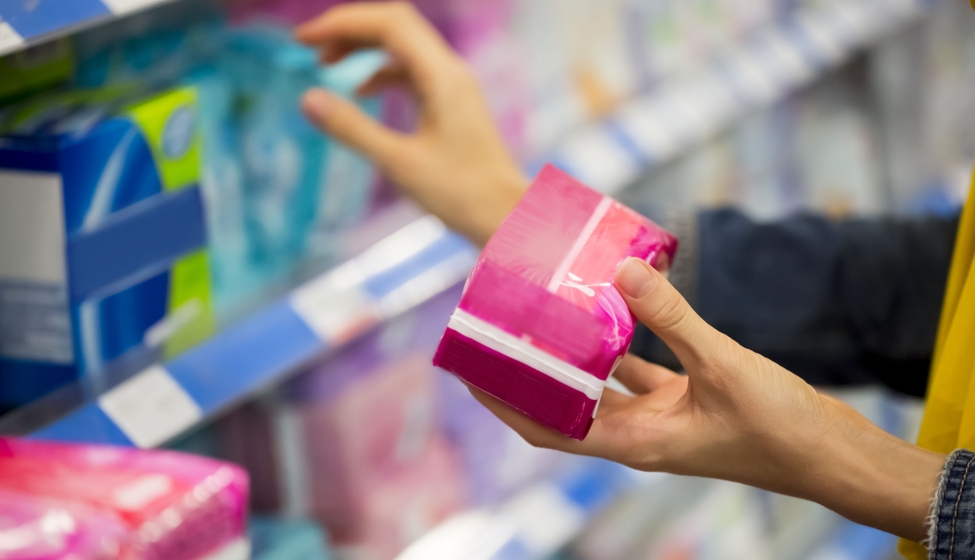 A customer grabbing a pack of menstrual pads from a shelf