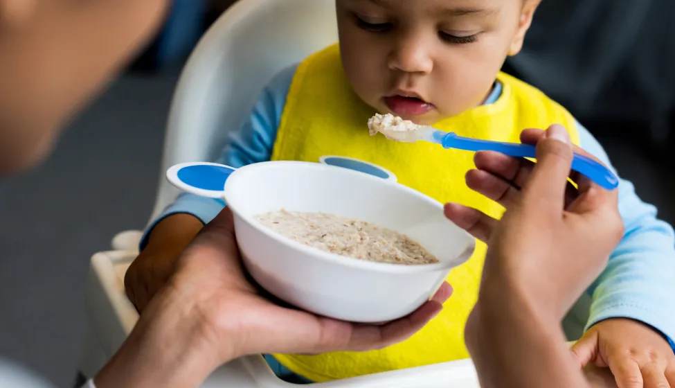 african american mother feeding little son with porridge at home