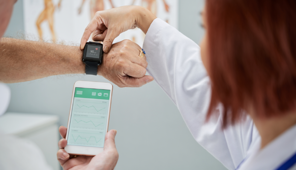 Medical professional holding a patient's smart watch on their wrist while reading vitals on her cell phone 