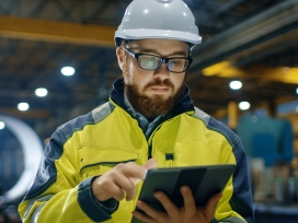 Inspector holds a clipboard and wears a hard hat in a factory setting. Exponent provides scientific and engineering risk assessments.