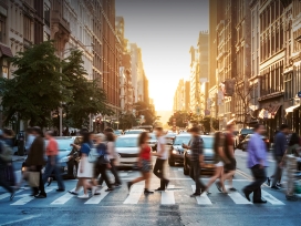 A crowd of people use a cross walk in a large city. Exponent helps build more inclusive technologies for all.