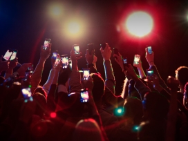 Crowd holds up cell phones at concert. Exponent provides technical engineering support for electronic device development.